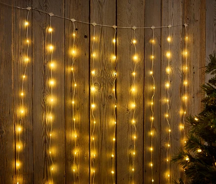 Ahşap bir arka planın önünde asılı ışık zincirleri, bir Noel ağacının yanında.