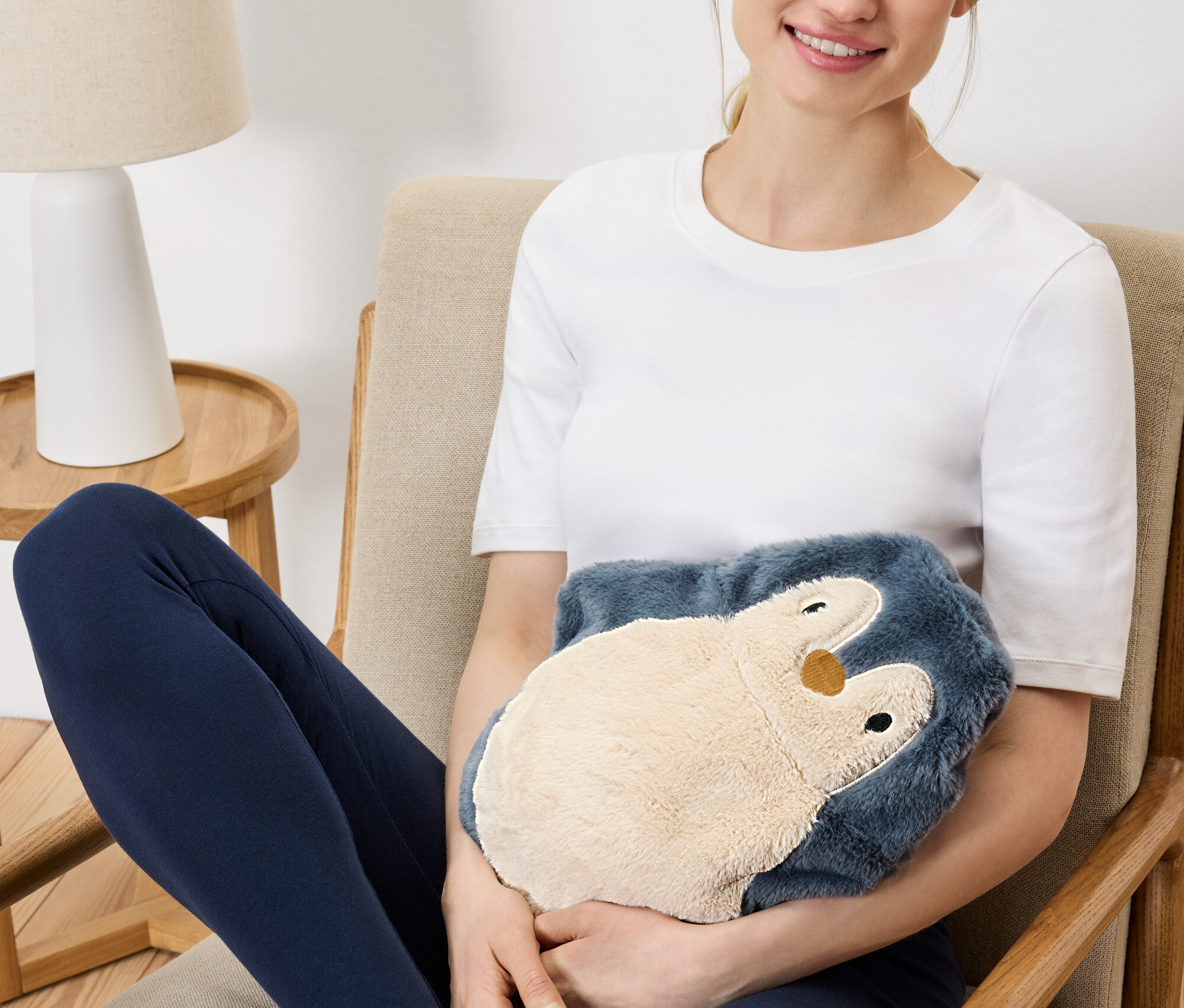 Kadın koltukta oturuyor ve peluş penguen ısıtıcısı tutuyor.