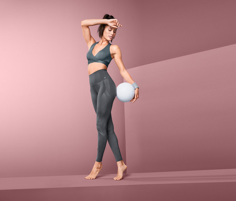 Kadın Bodyforming Spor Taytı ve spor sutyeni ile poz veriyor, beyaz bir top tutuyor.