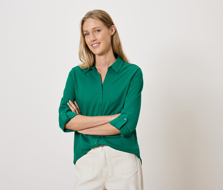 Kadın yeşil gömlek ve beyaz pantolonla kolları çapraz şekilde poz veriyor.
