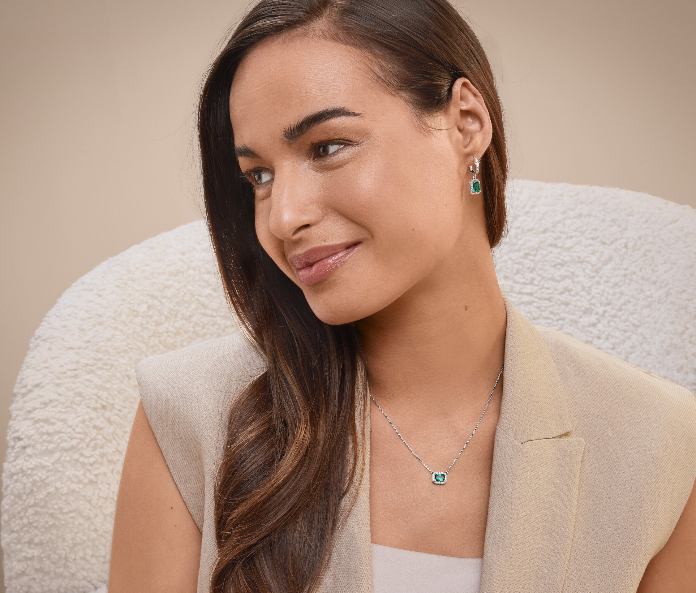 Bir kadın sandalyede oturuyor, kolye ve küpe takıyor.