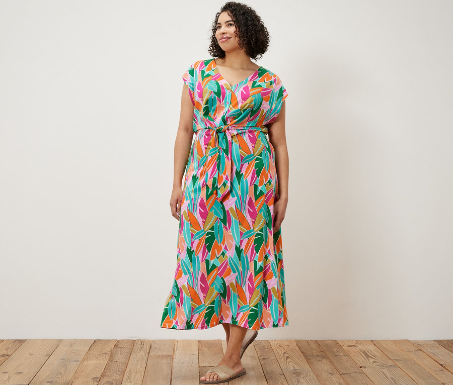 Bir kadın ayakta duruyor ve düğümlü jarse elbise giyiyor.