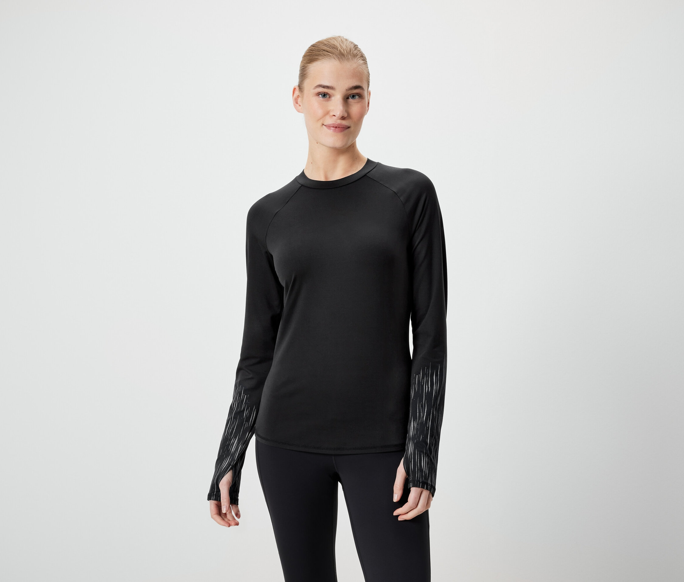 Kadın, siyah uzun kollu bir tişört ve siyah tayt giyiyor.