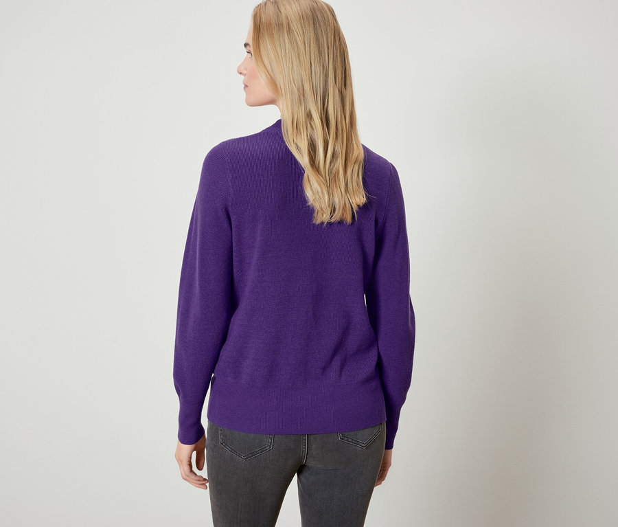 Arkadan görünüşü, mor bir kazak ve gri kot pantolon giyen sarışın bir kadın.