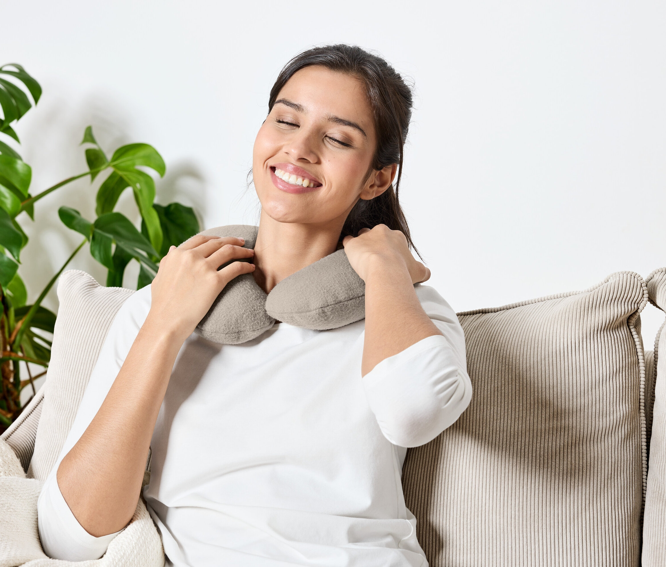 Kadın gözleri kapalı bir şekilde kanepede oturuyor ve boynunda gri bir yastık var.