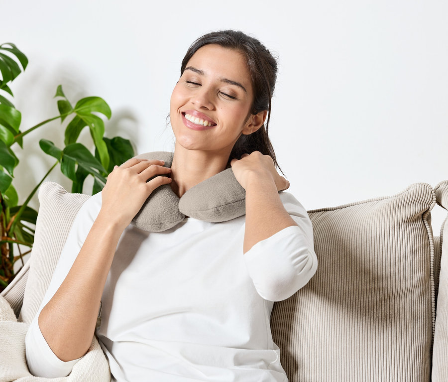 Kadın gözleri kapalı bir şekilde kanepede oturuyor ve boynunda gri bir yastık var.