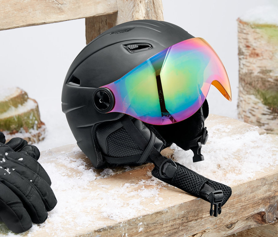 Hardshell vizörlü kayak ve snowboard kaskı ahşap bir bankta duruyor. Yanında siyah eldivenler var.