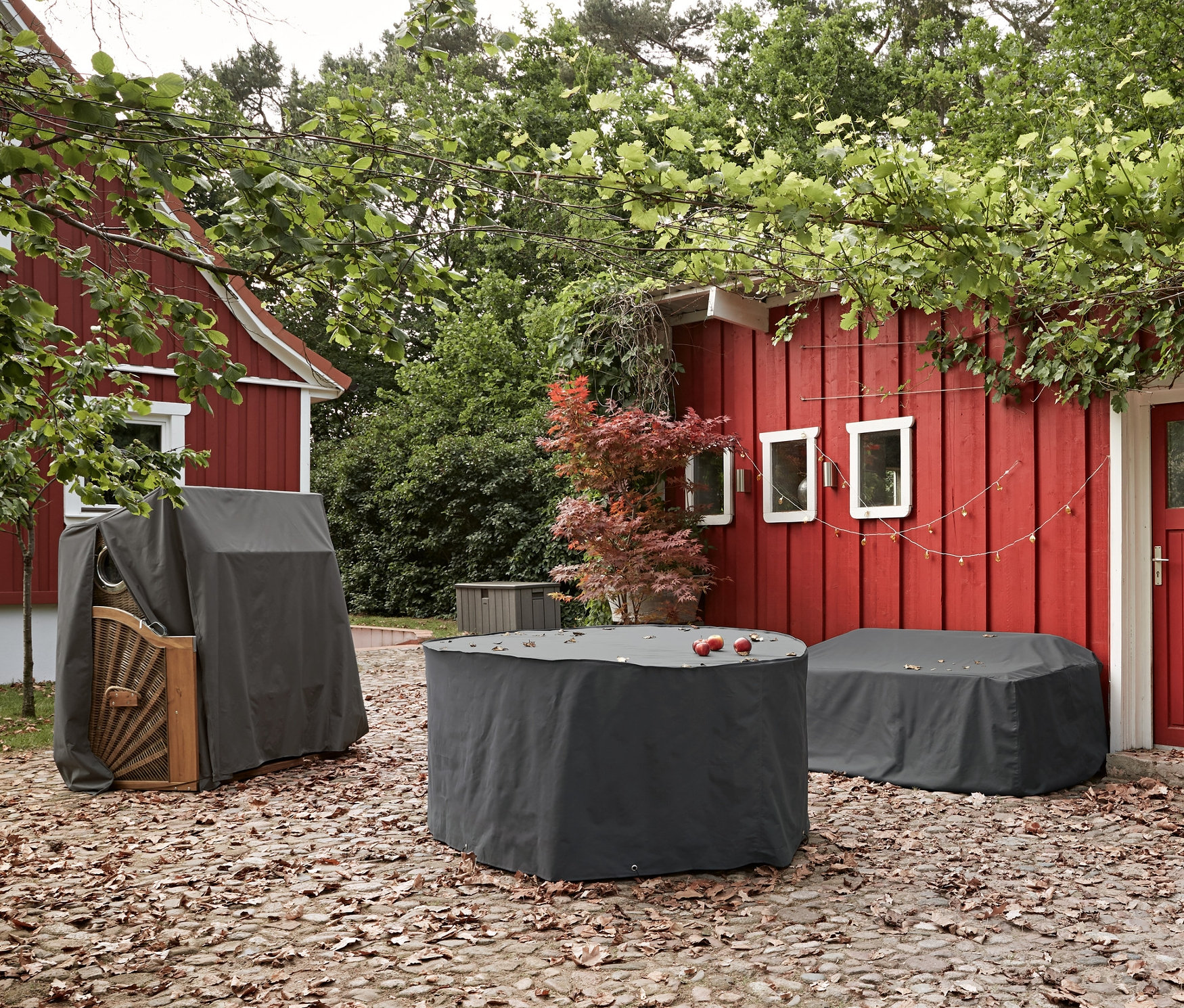 Taş döşeli bir terasta yemek masası takımı, bahçe mobilyası "bahçe koltuğu" ve plaj sepeti için premium koruyucu örtüler bulunmaktadır.