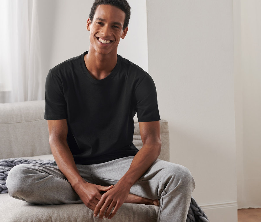 Adam kanepede oturuyor, üzerinde siyah tişört ve gri eşofman altı var.