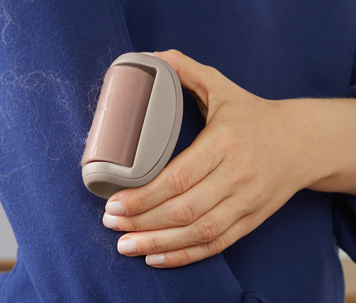 Kadın, mavi bir kazağın üzerindeki tüyleri tüy toplama rulosuyla temizliyor.