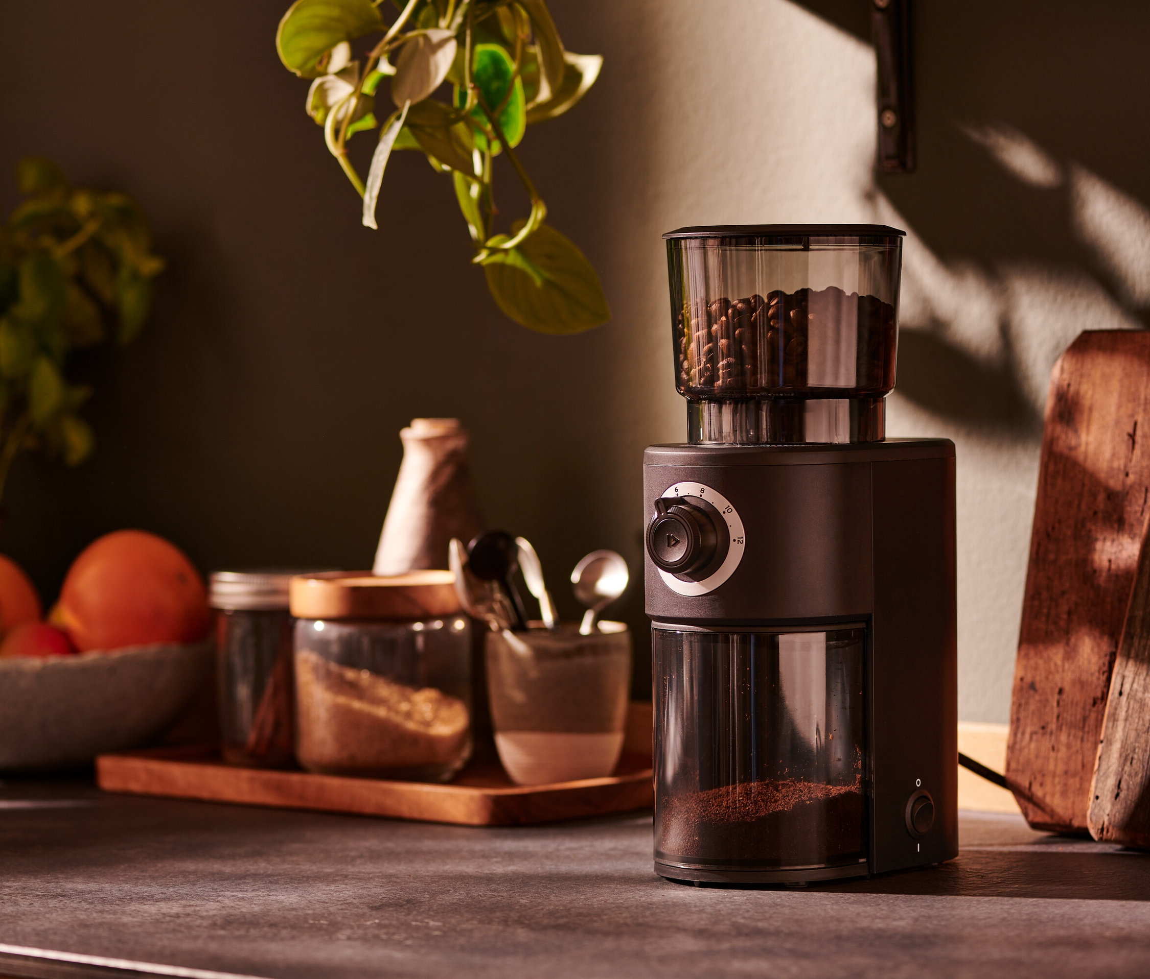 Kahverengi, elektrikli bir kahve değirmeni, mutfak tezgahında baharat kavanozlarının yanında duruyor.