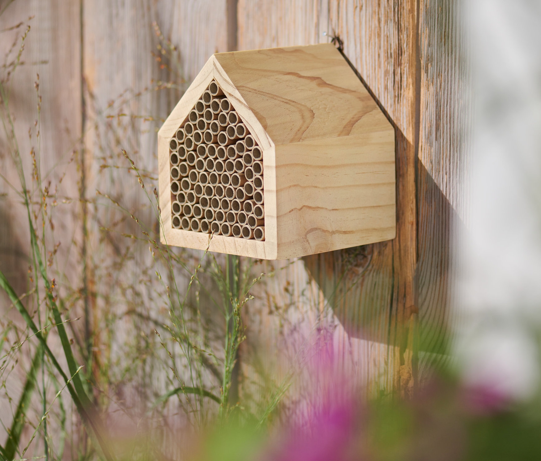 Ahşap bir çitin üzerine monte edilmiş, ev şeklinde ahşap bir böcek oteli.