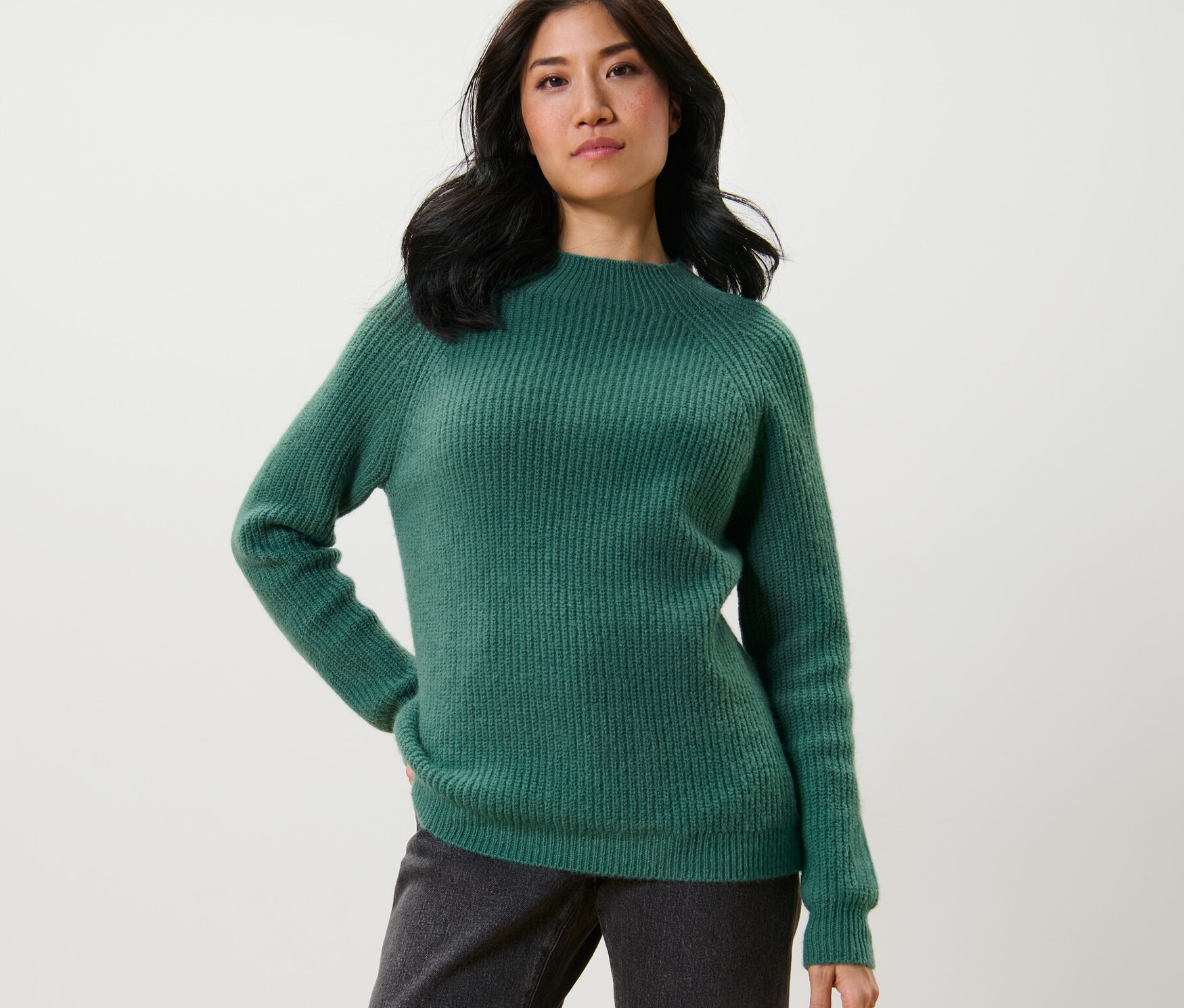 Kadın, Yeşil Yarım Boğazlı Kalın Örgülü Kazak ve koyu renk pantolonla poz veriyor.