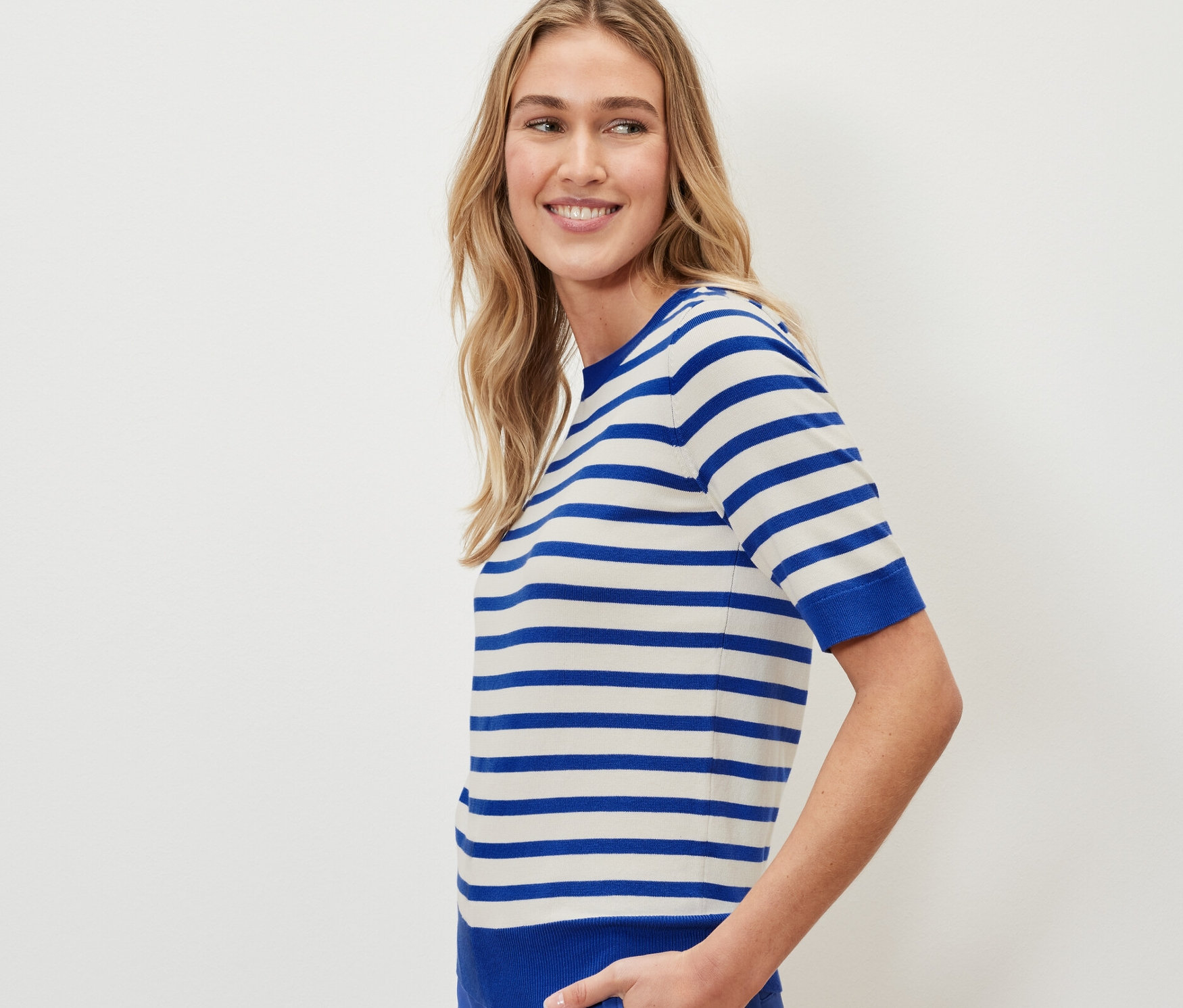 Kadın çizgili ince örgülü bir kazak ve mavi pantolon giyiyor.