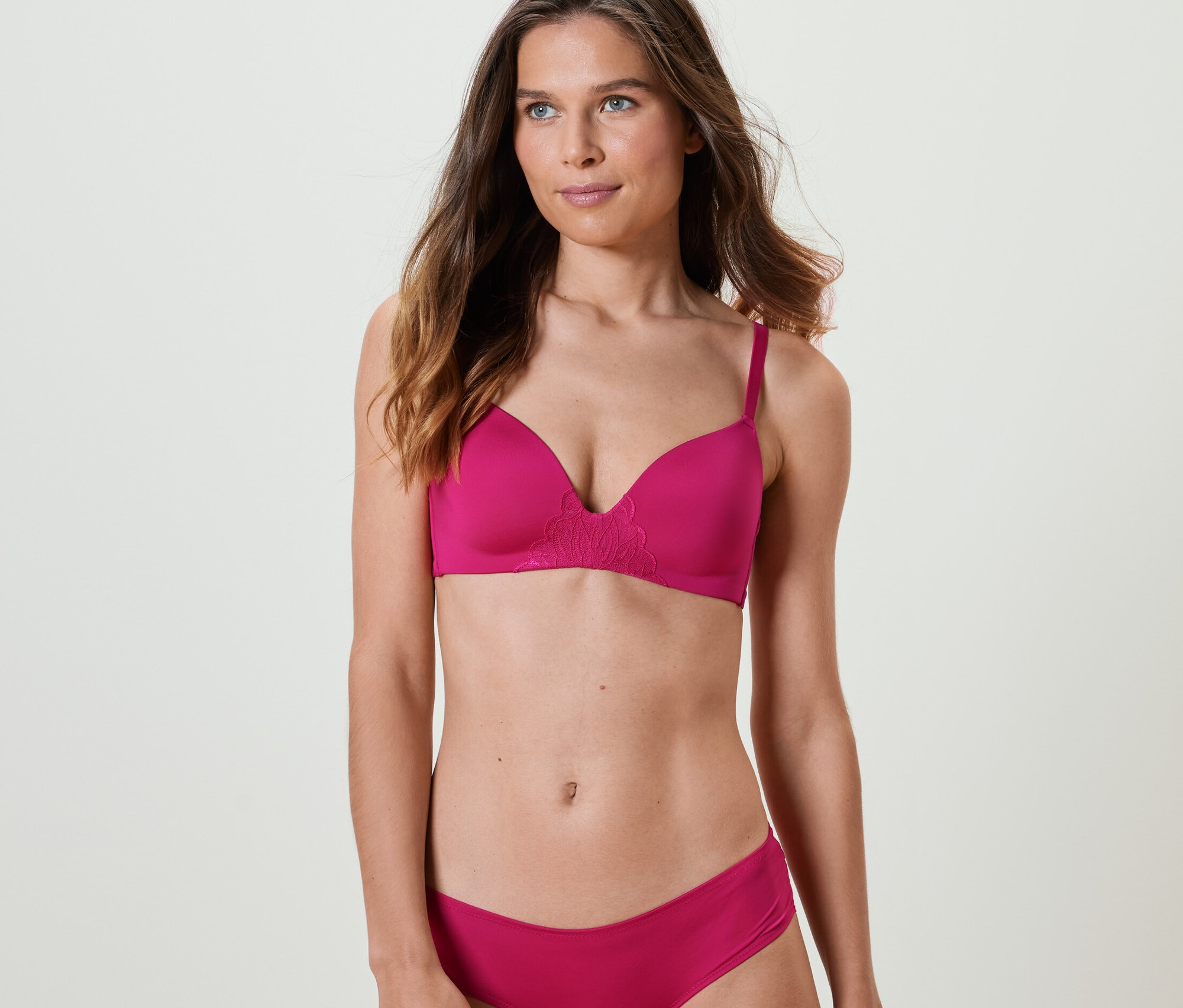 Kadın fuşya rengi, yumuşak kuplu bir sütyen ve külot giyiyor.