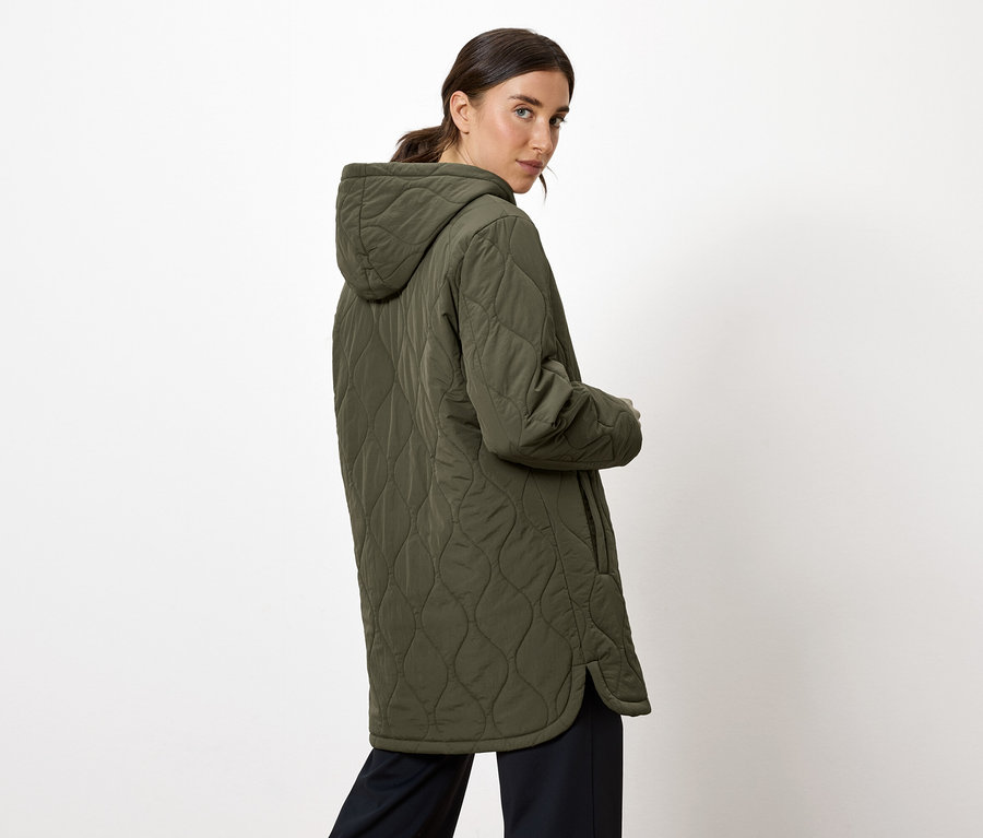 Bir kadın omzunun üzerinden bakıyor ve kapüşonlu zeytin yeşili kapitone bir mont giyiyor.