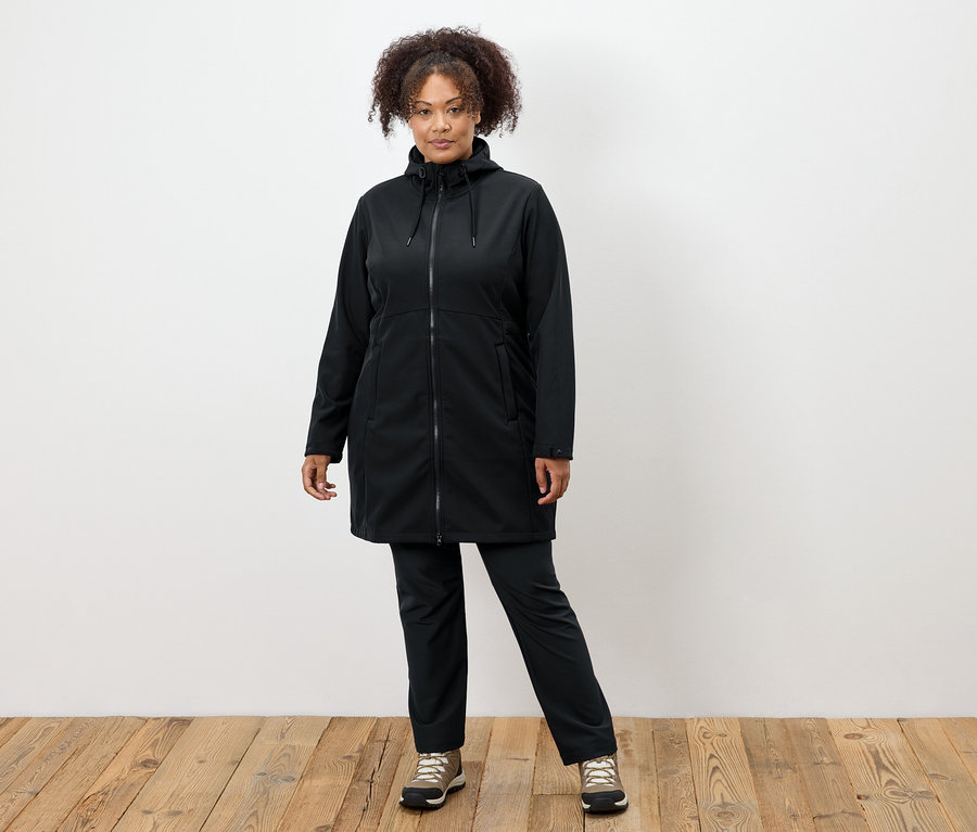 Siyah montlu ve pantolonlu bir kadın ahşap zeminde duruyor.