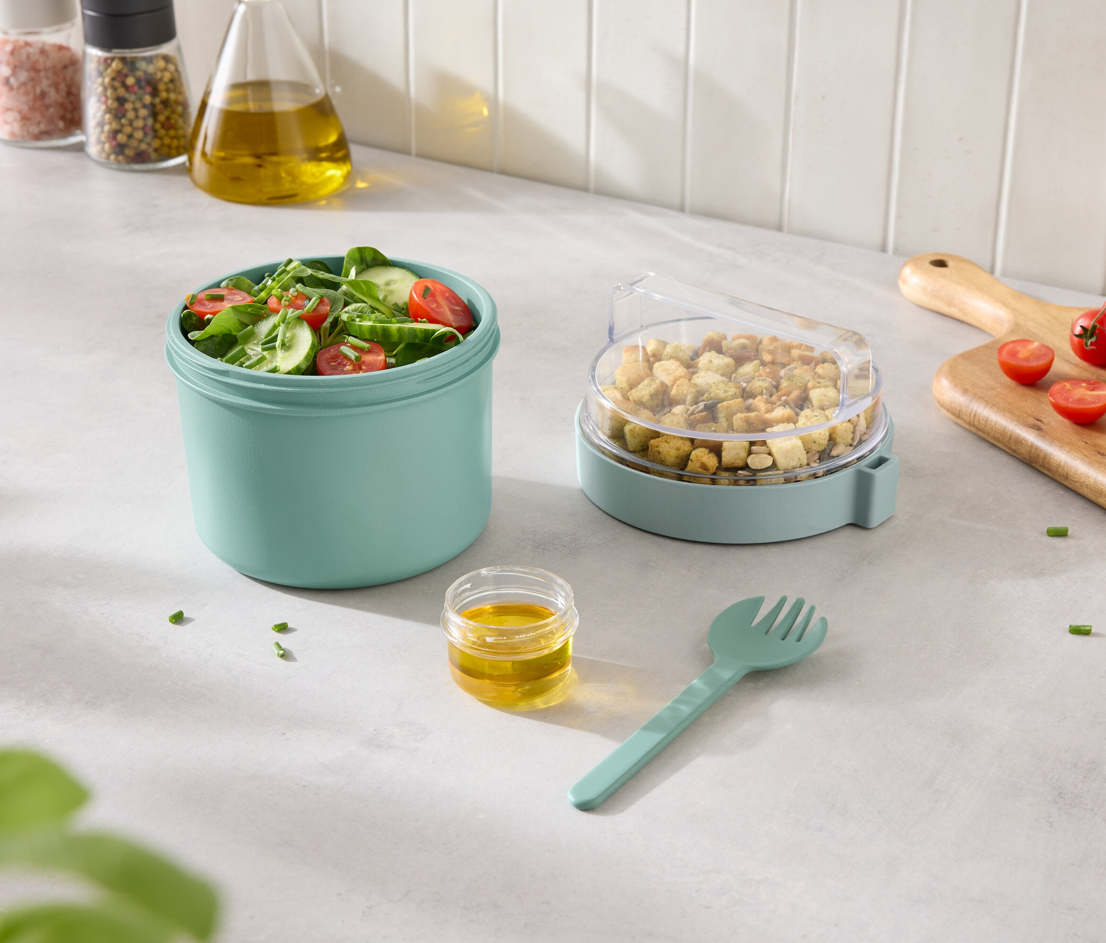 Turkuaz bir kapta karışık salata, şeffaf kapaklı bir kapta krutonlar, yanında sos ve çatal.