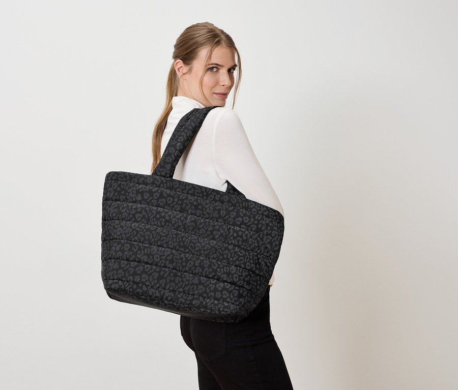 Omuzunda büyük, kapitone leopar desenli bir tote çanta olan kadın.