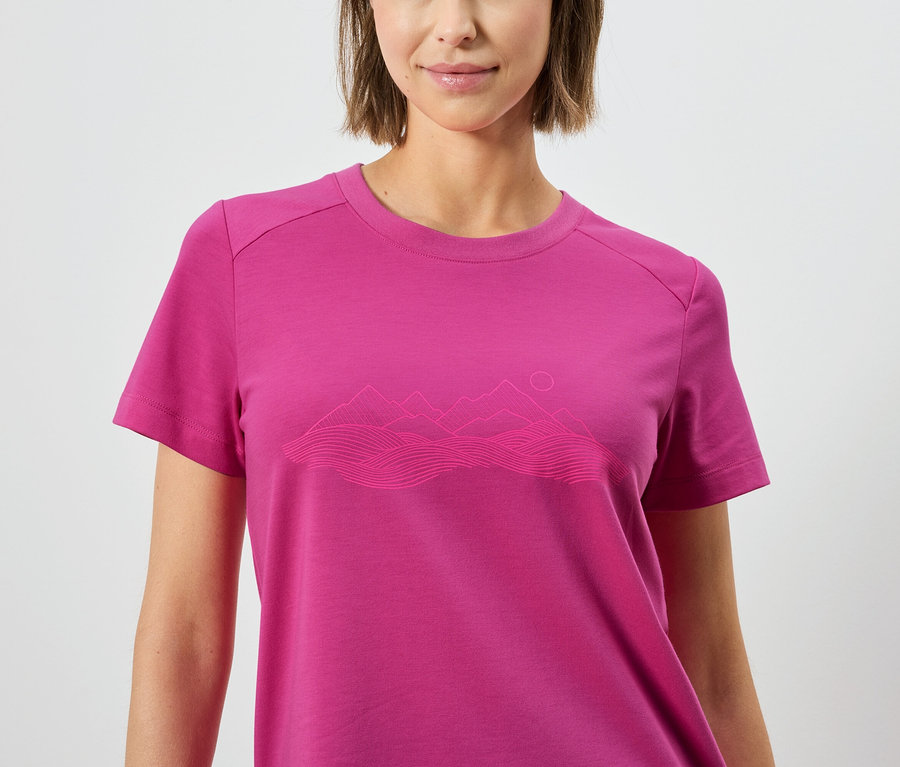 Kadın üzerinde dağ manzarası deseni olan pembe bir tişört giyiyor.