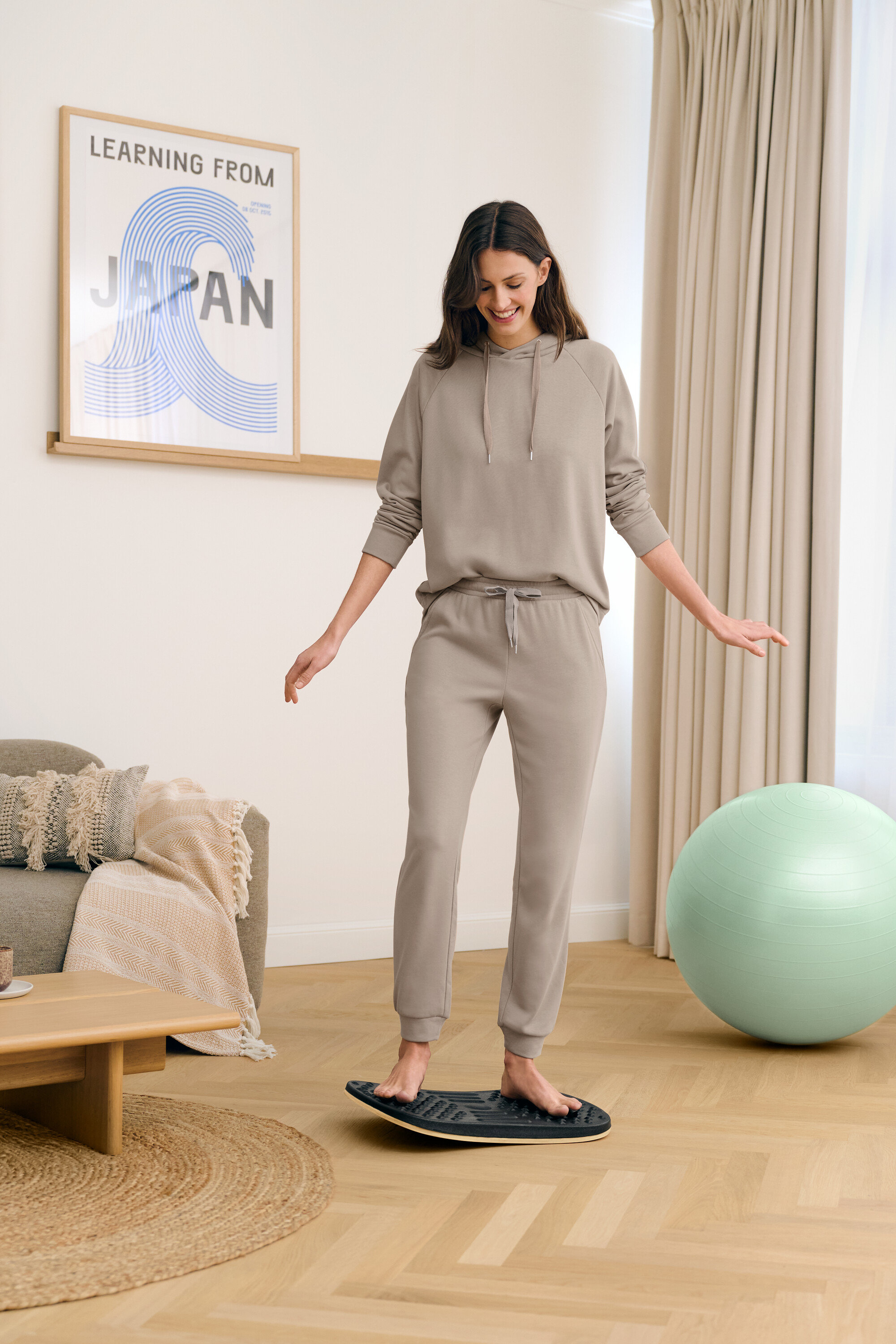 Bir kadın oturma odasında çıplak ayakla denge tahtası üzerinde duruyor.