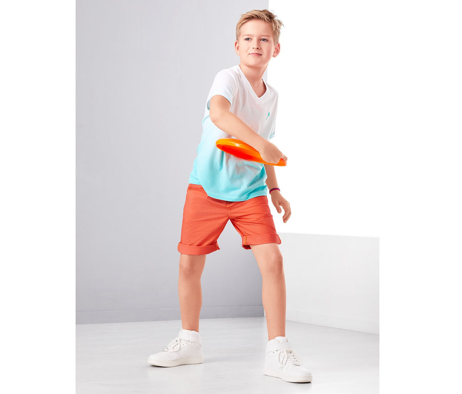 Oğlan turuncu disk atıyor. Şort giyiyor.