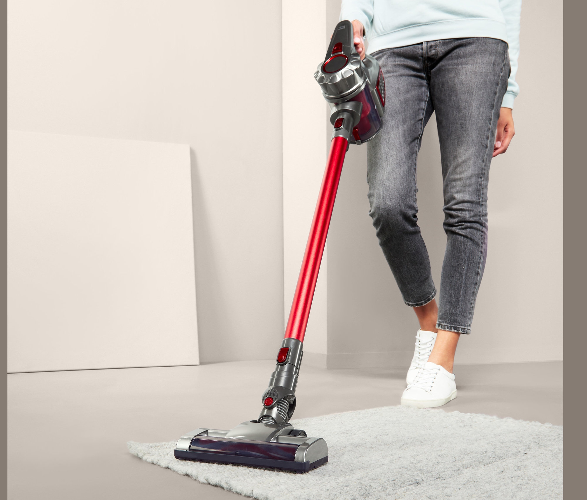 Kadın, kablosuz elektrikli süpürgeyle tüylü halıyı süpürüyor.