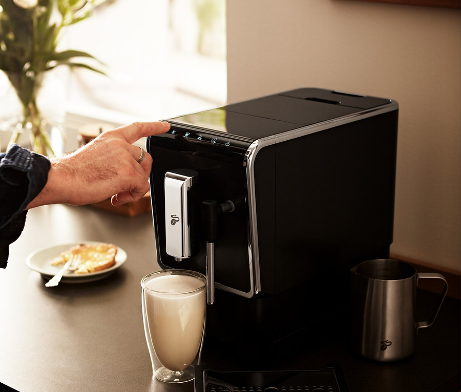 Adam, antrasit renkli »Esperto Latte« Tchibo Tam Otomatik Kahve Makinesinin üzerinde bir düğmeye basıyor.