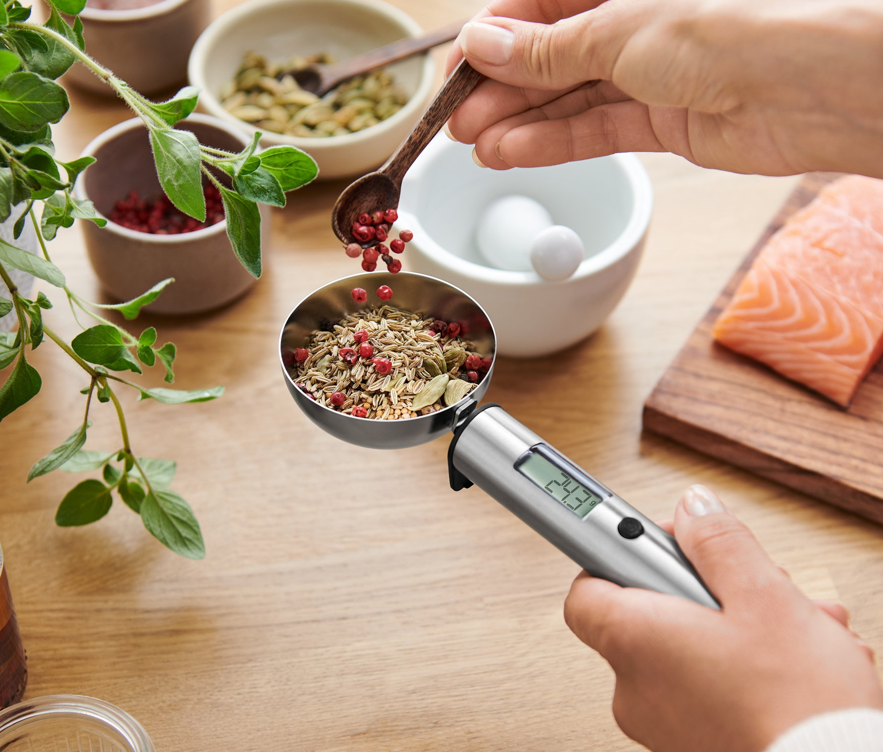 Kadın, iki somon filetosunun üzerinde dijital kaşık terazisine baharat ekliyor.