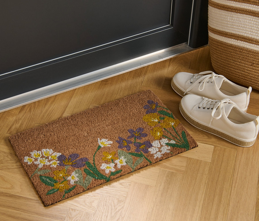 Çiçek desenli bir Hindistan cevizi paspası bir kapının önünde duruyor.