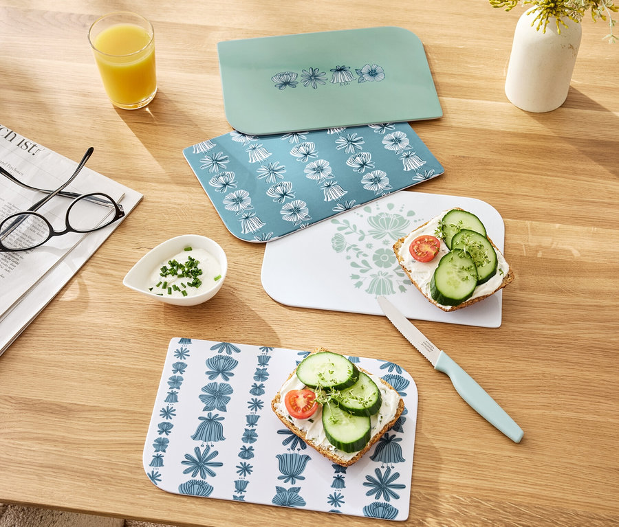 Dört adet kahvaltı tahtası ahşap bir masa üzerinde duruyor, ikisi sandviçli. Ayrıca bir bardak portakal suyu, bir kase sos ve bir bıçak da görülebilir.