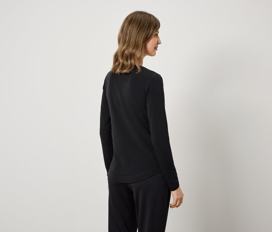 Arkadan görünen bir kadın, siyah uzun kollu bir bluz ve siyah pantolon giyiyor.