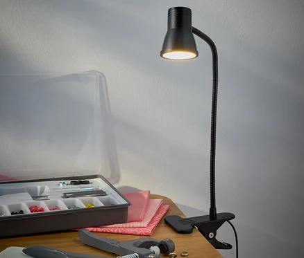 Siyah LED kıskaçlı lamba, masanın üzerinde bir dikiş setinin yanında duruyor.