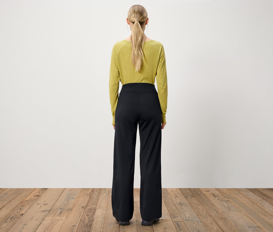 Arkadan at kuyruğu yapılmış sarı saçlı, zeytin yeşili uzun kollu bir bluz ve siyah, geniş paçalı pantolon giyen bir kadın görülüyor.