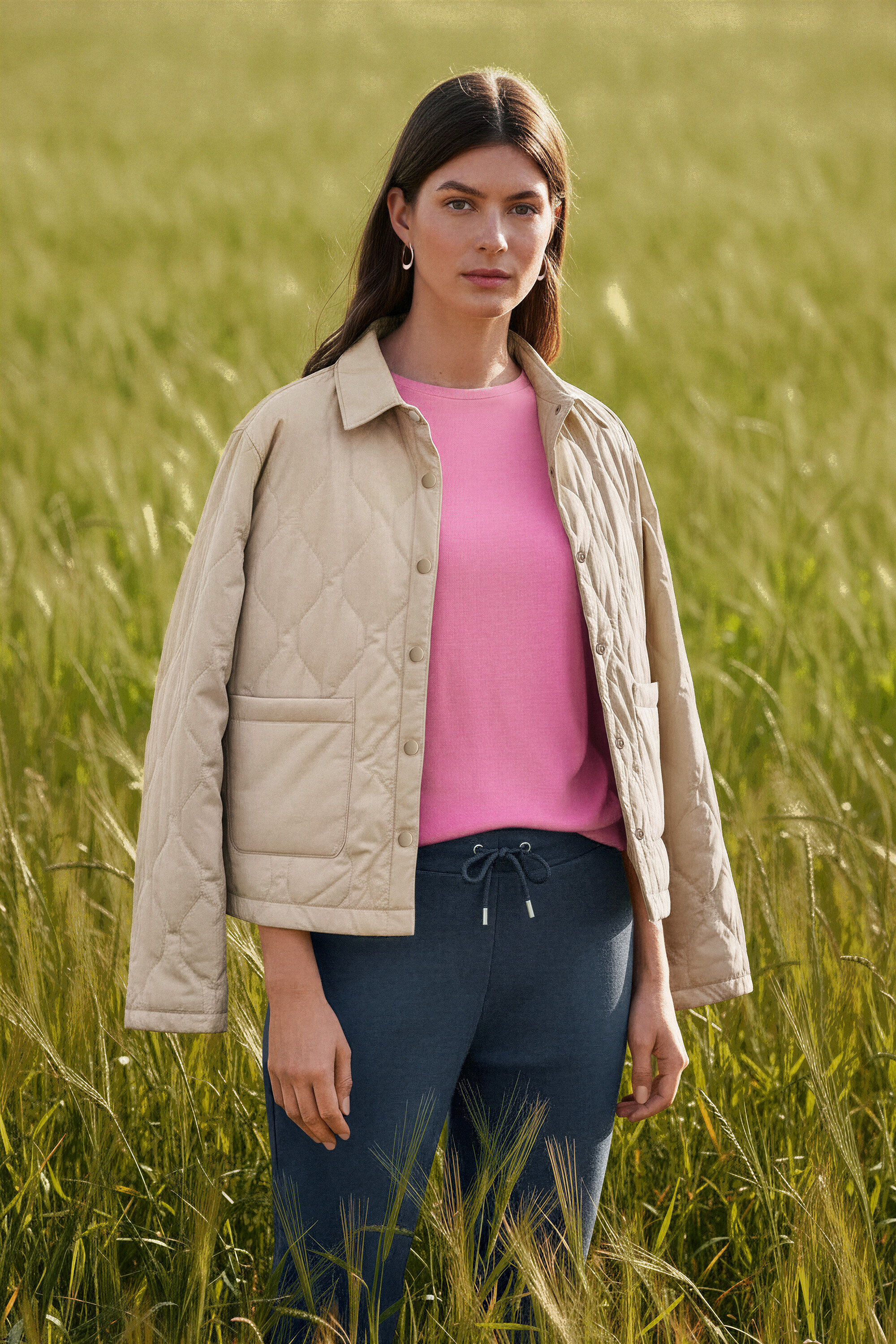 Tarlada duran ve Dalga Halka Küpe takan kadın.