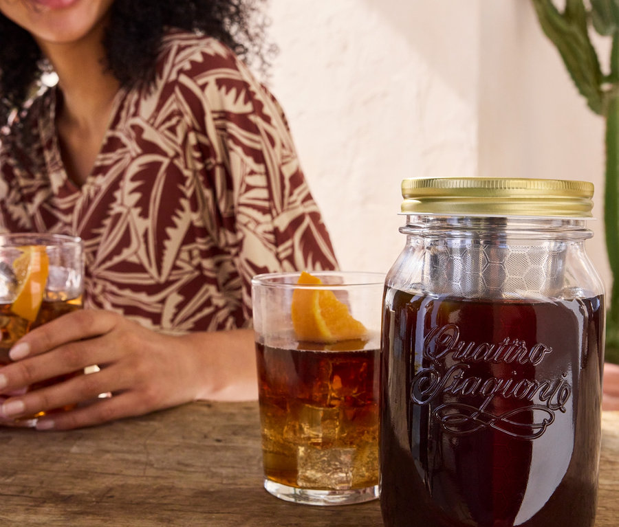 Kadın, Soğuk demleme hazırlayıcı "BrewJar" ve baskılı jarse elbisenin yanında bir bardak içecek tutuyor.