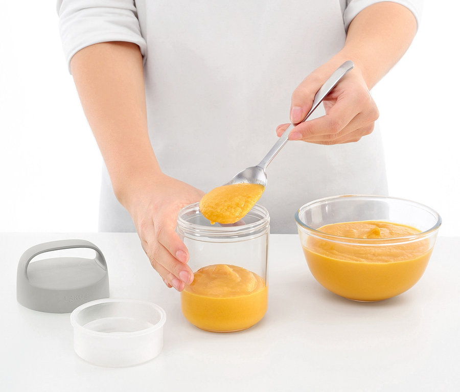 Kişi, Taşınabilir Atıştırmalık Kutusunu bir kaşıkla turuncu sıvı ile dolduruyor. Kutunun yanında turuncu sıvı içeren bir kase var.