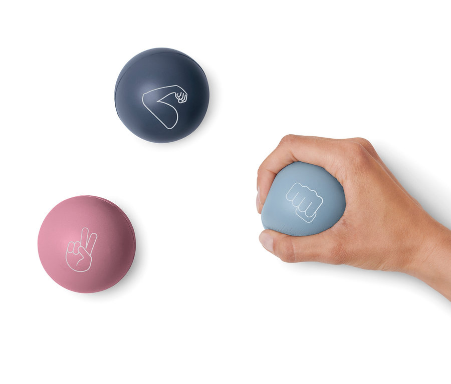 Bir el, yumruk sembolü olan mavi bir stres topu tutuyor. Beyaz bir arka planda, barış sembolü olan pembe bir top ve pazı sembolü olan koyu mavi bir top var. 3 Adet Stres Topu.