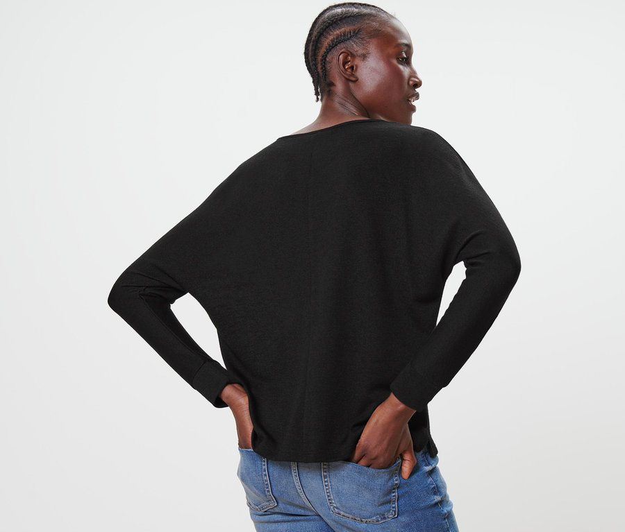 Siyah Yarasa Kol Bluz ve mavi kot pantolon giyen bir kadın arkadan poz veriyor.