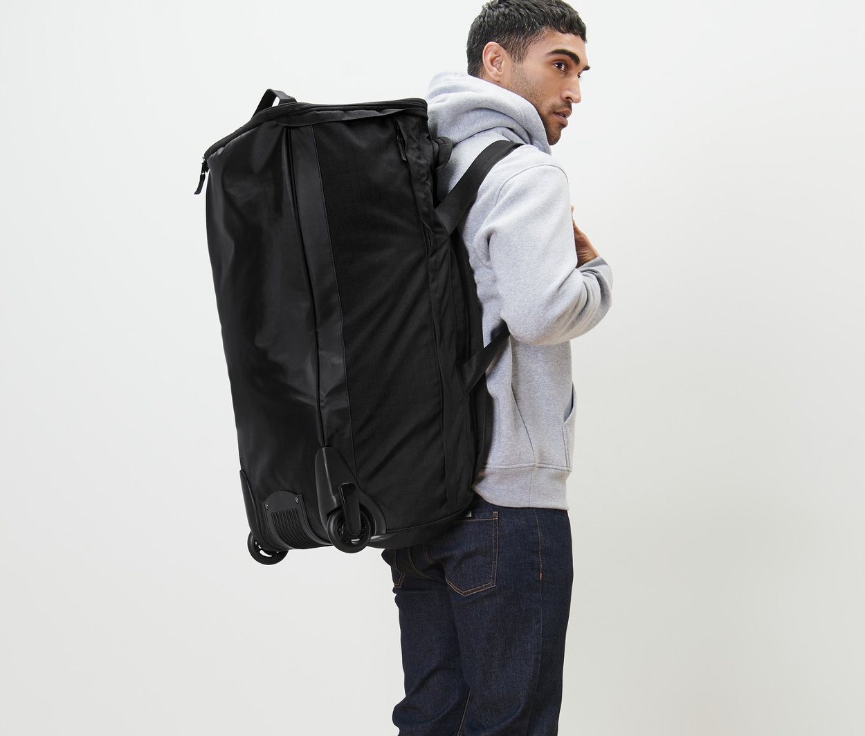 Adam sırtında tekerlekli çantayı taşıyor.
