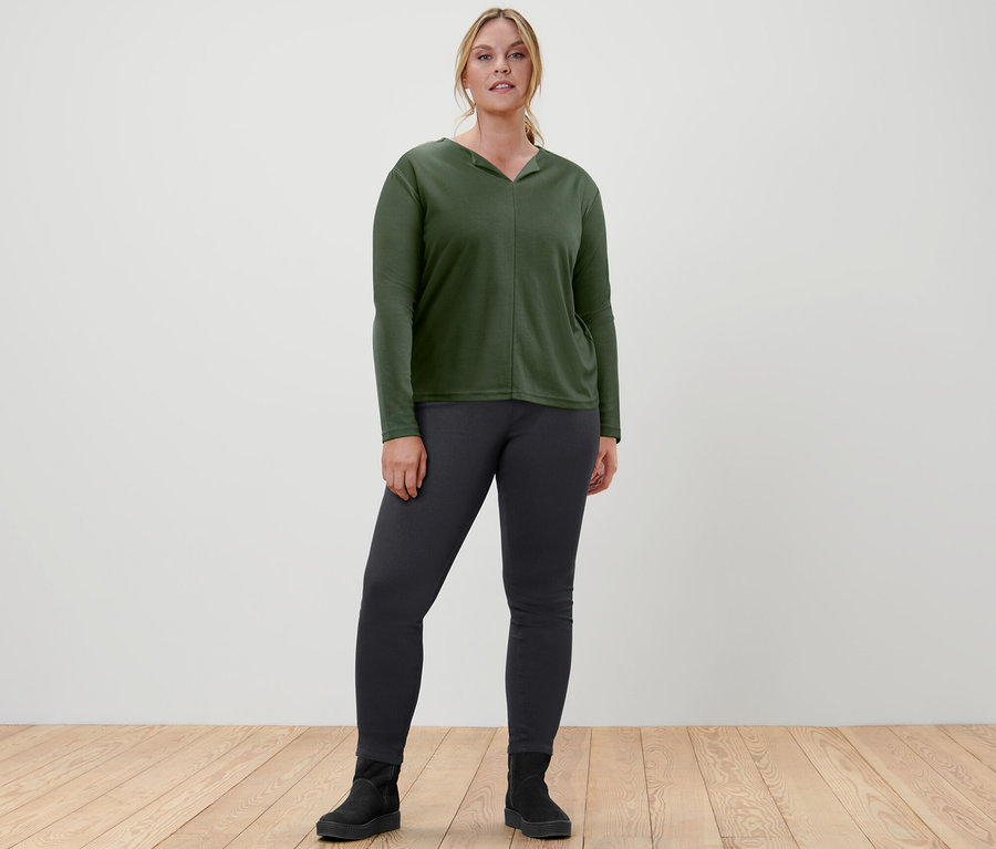 Kadın koyu yeşil bluz ve jegging pantolonla poz veriyor.