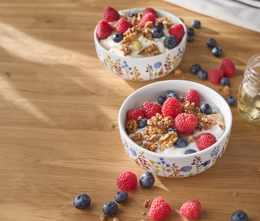 Ahşap bir masanın üzerinde ahududu, yaban mersini ve fındık bulunan iki kase yoğurt.