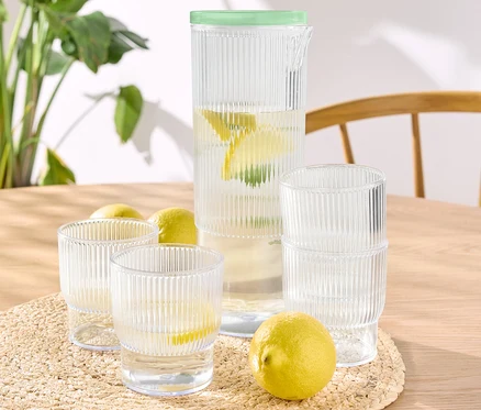 Bir masanın üzerinde 4 adet plastik bardak ve sürahi bulunmaktadır, bazıları su ve limonla doldurulmuştur.