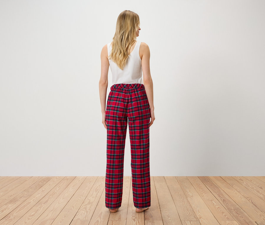 Bir kadın kameraya arkası dönük duruyor, beyaz bir atlet ve kırmızı kareli bir pantolon giyiyor.