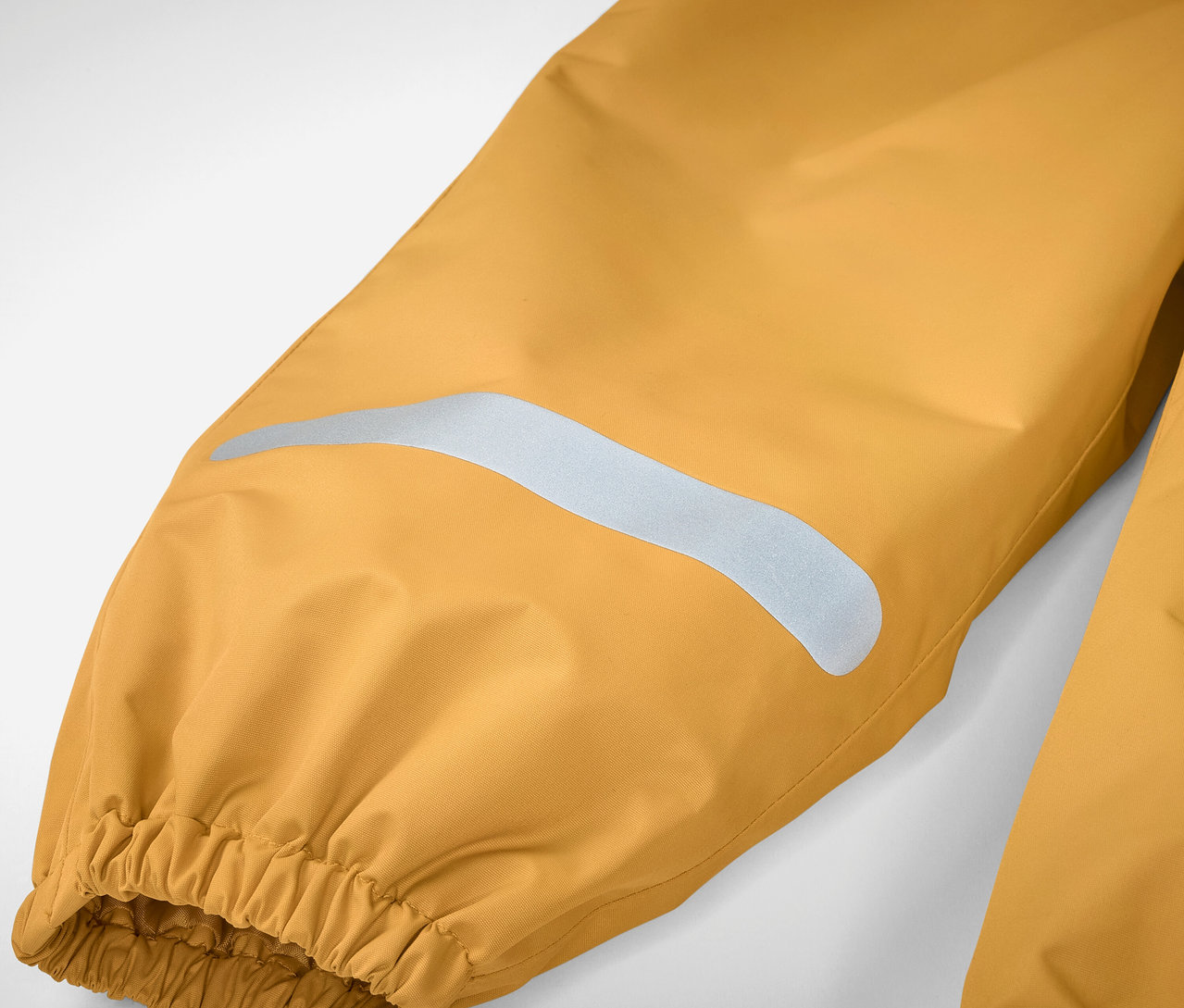 Reflektörlü şerit ve lastikli kenara sahip sarı renkli çocuk yağmurluğunun detayı.