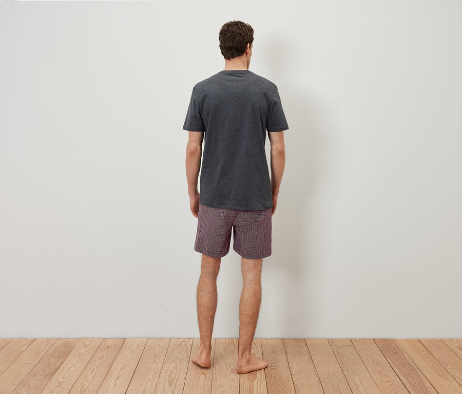 Sırtı kameraya dönük bir adam gri bir tişört ve kareli şort giyiyor.