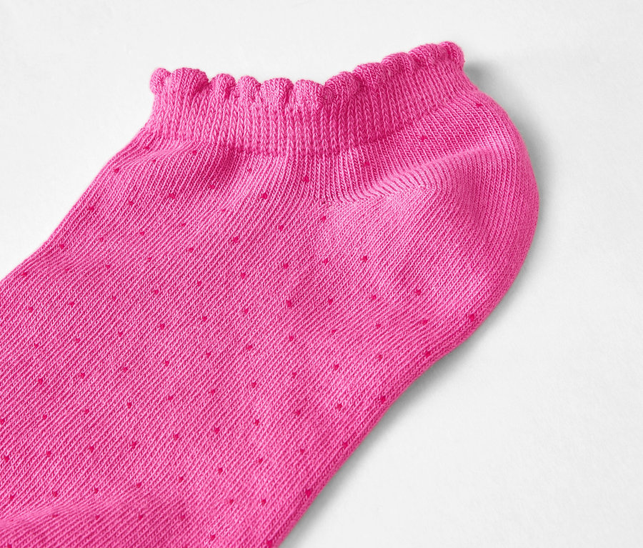 Beyaz bir arka planda fırfırlı kenarlı ve küçük noktalı tek bir pembe, kısa kesim çorabın yakın çekimi.