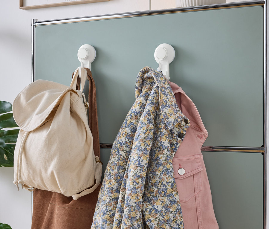 Bej kumaş çanta, kahverengi süet çanta, mavi çiçekli gömlek ve pembe kot ceket, nane yeşili dolap duvarında beyaz vantuzlu kancalara asılı.