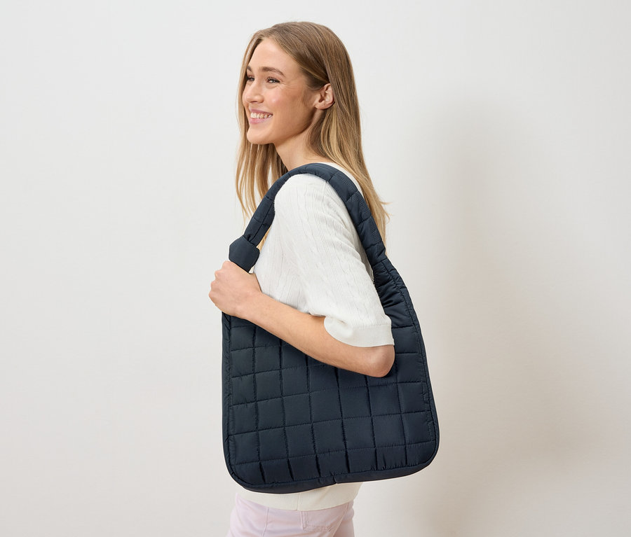 Kadın omuzunda lacivert, kapitone bir taşıma çantası taşıyor.