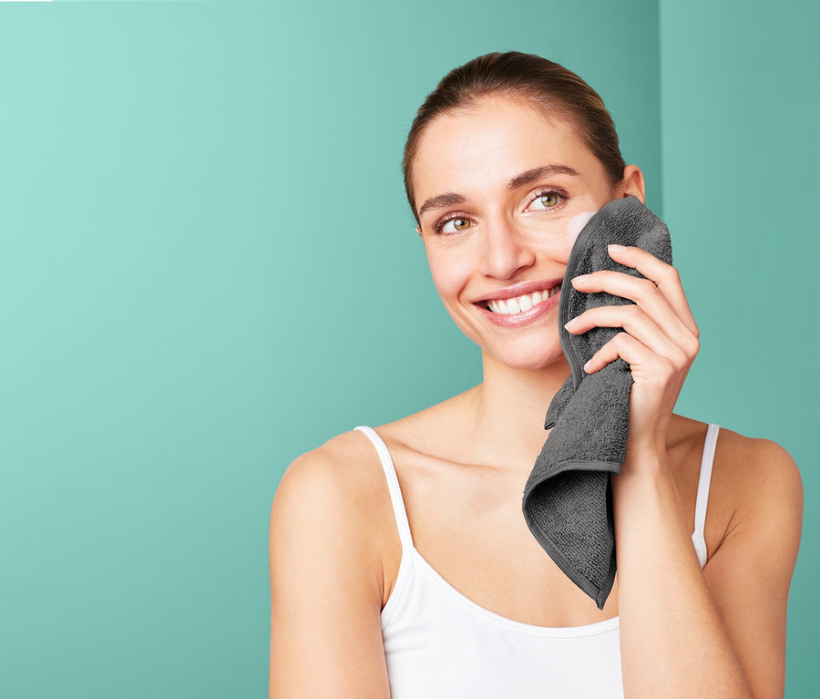 Kadın yüzünü gri bir mikrofiber makyaj havlusuyla temizliyor.